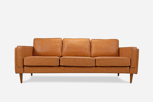 The Albany Sofa is a mid-century modern tan leather couch with three seat and back cushions, plus wooden legs, displayed against a plain white background.