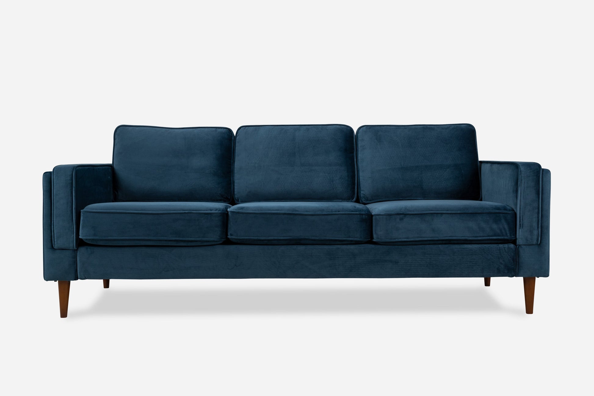 The Albany Sofa is a modern dark blue velvet piece with three seat cushions, three back cushions, and wooden legs, shown against a plain white background.