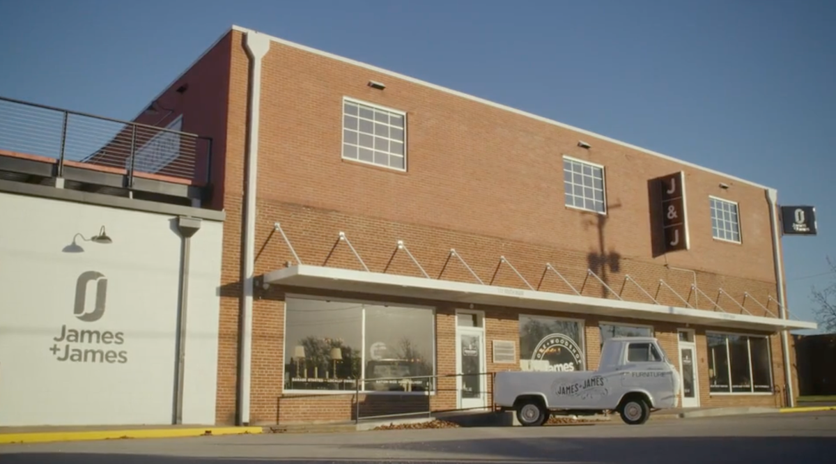 A two-story brick building with a vintage pickup truck parked outside. The building features large windows and has "James + James" signage. A smaller adjacent building displays the same branding. The scene is under a clear blue sky.