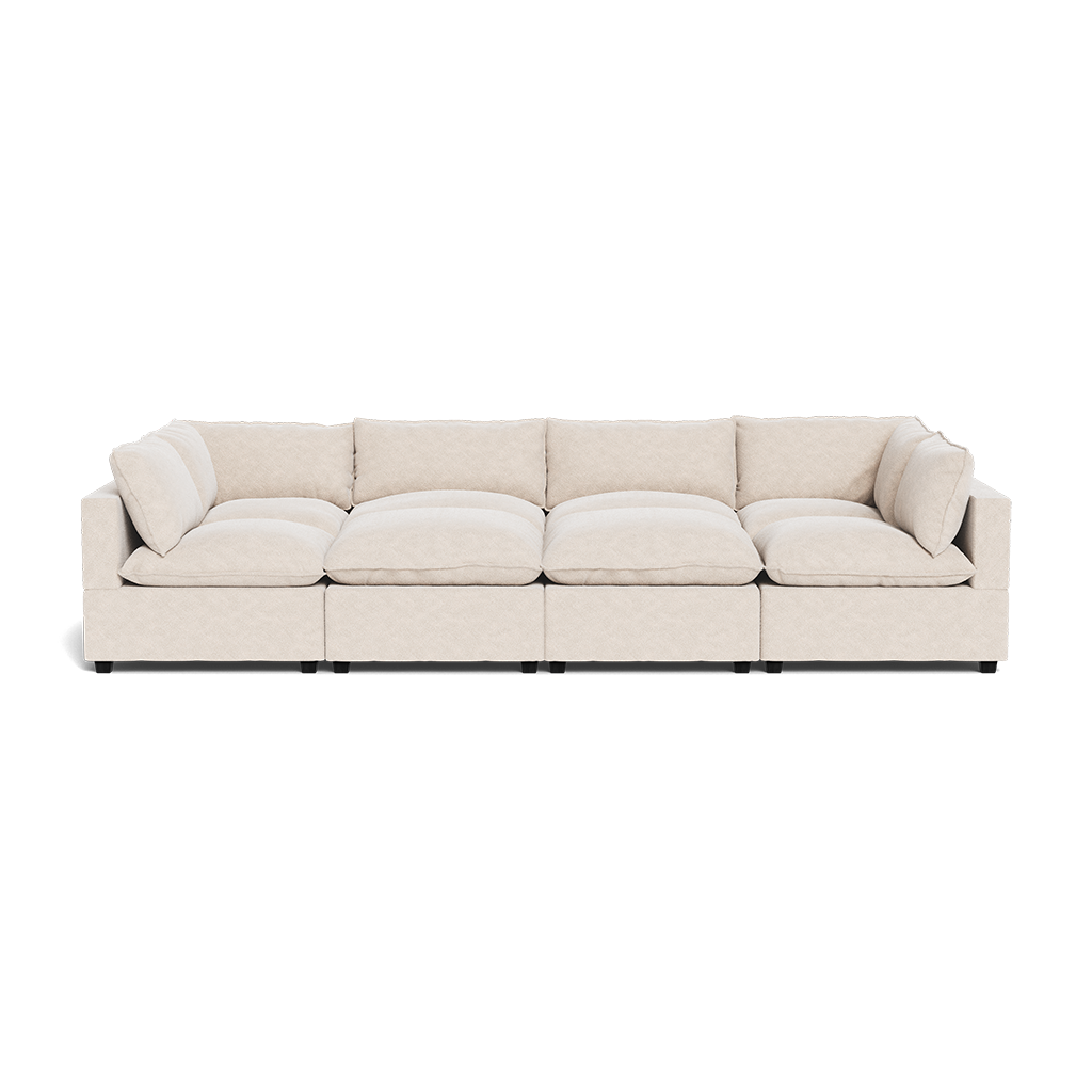 The Kova Pillow Cushion Grand Pit is a long, light beige modular sofa with deep seats, wide cushions, and low armrests, arranged in a straight line on a plain white background.