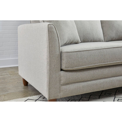 A close-up of the Kodie 76.5" Upholstered Sleeper Sofa in light gray, featuring elegant wooden legs. The sofa is positioned against a white brick wall, with part of a geometric patterned rug visible on the floor.