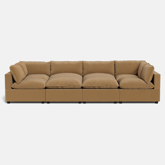 The Kova Pillow Cushion Grand Pit is a modern tan sectional sofa featuring four large seat cushions, plush back and side pillows, and a low rectangular design with short black legs, shown against a plain white background.