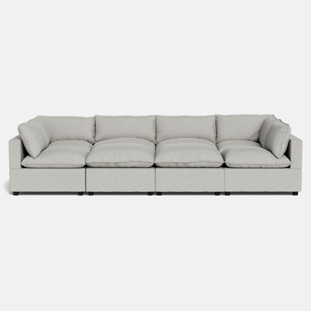 The Kova Pillow Cushion Grand Pit is a modern, light gray four-seat sofa featuring plush cushions and wide armrests, shown against a plain white background.