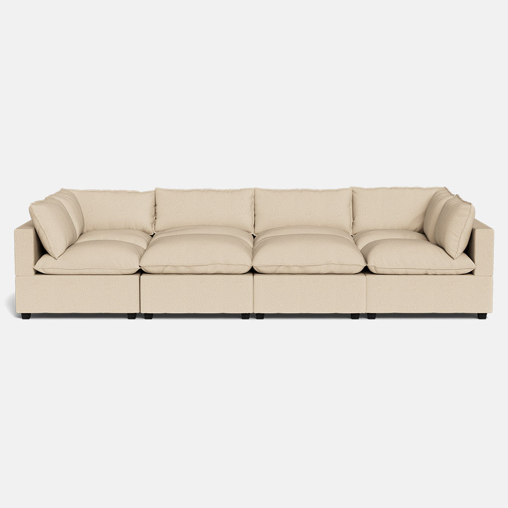 The Kova Pillow Cushion Grand Pit is a modern beige sectional sofa with four seat cushions and plush back pillows, shown against a plain white background.