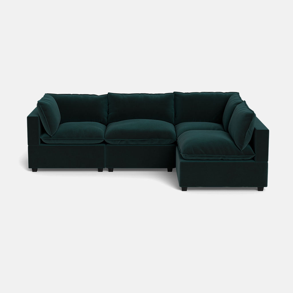 The Kova Pillow Cushion L-Shape is a modern, dark green sectional sofa with plush cushions and low armrests, shown against a plain white background.