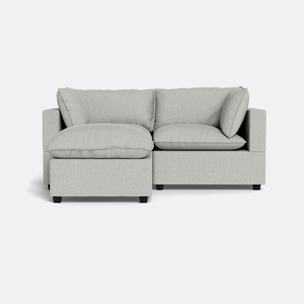 A modern Kova Pillow Cushion Sofa 86" in light gray, featuring plush cushions and a left-side chaise with ottoman, displayed against a plain white background.