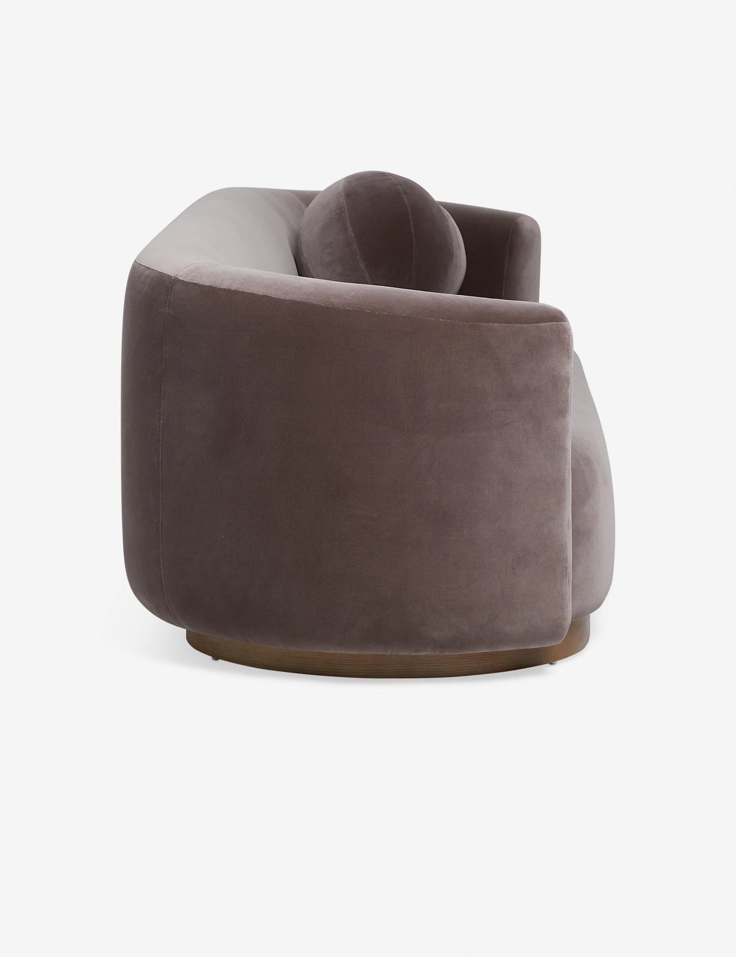 Introducing the Lowry Sofa: a contemporary, curved piece upholstered in dark gray velvet with plush cushioning. Its elegant, rounded silhouette is captured from a side angle, showcasing the smooth fabric and modern design.