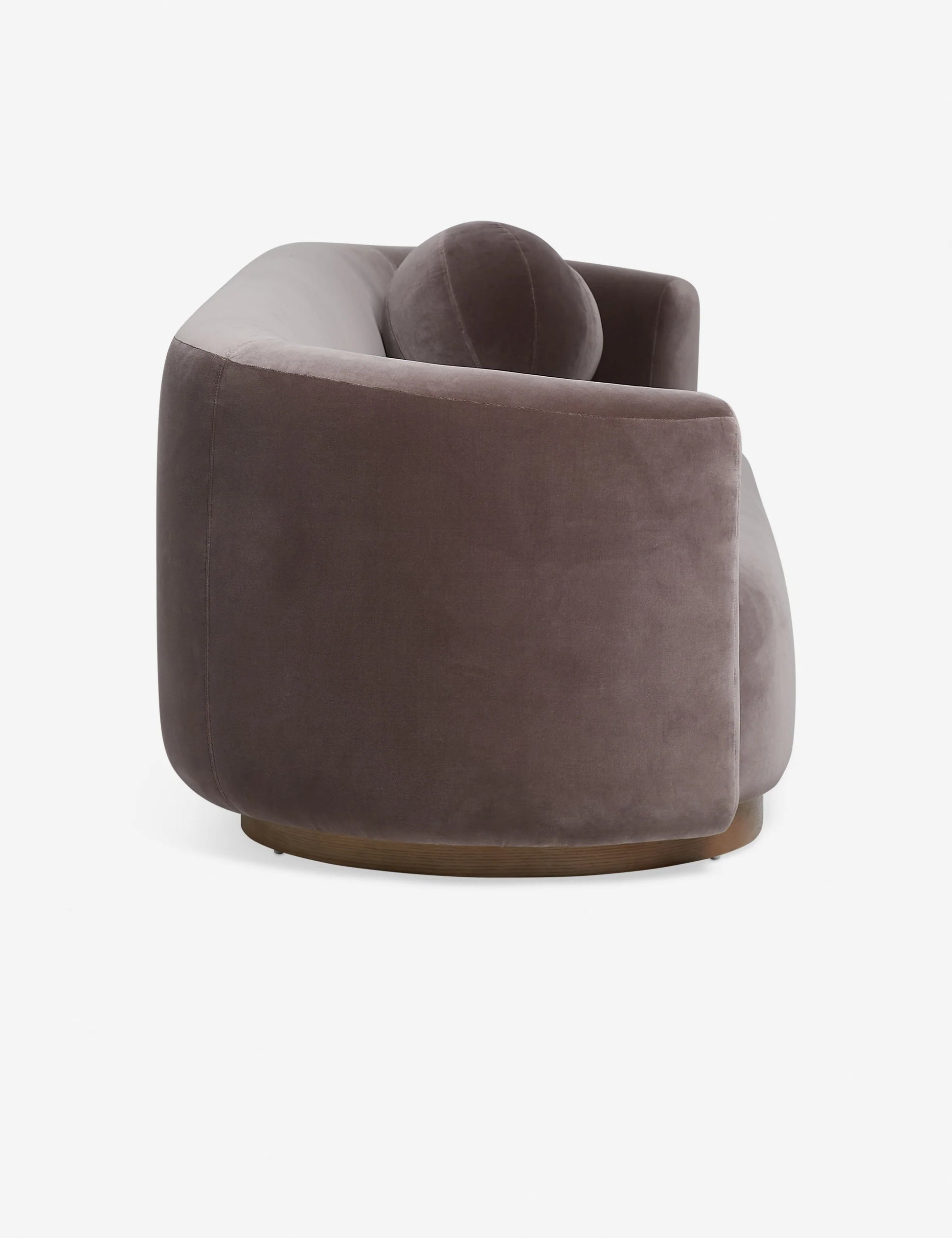 Introducing the Lowry Sofa: a contemporary, curved piece upholstered in dark gray velvet with plush cushioning. Its elegant, rounded silhouette is captured from a side angle, showcasing the smooth fabric and modern design.