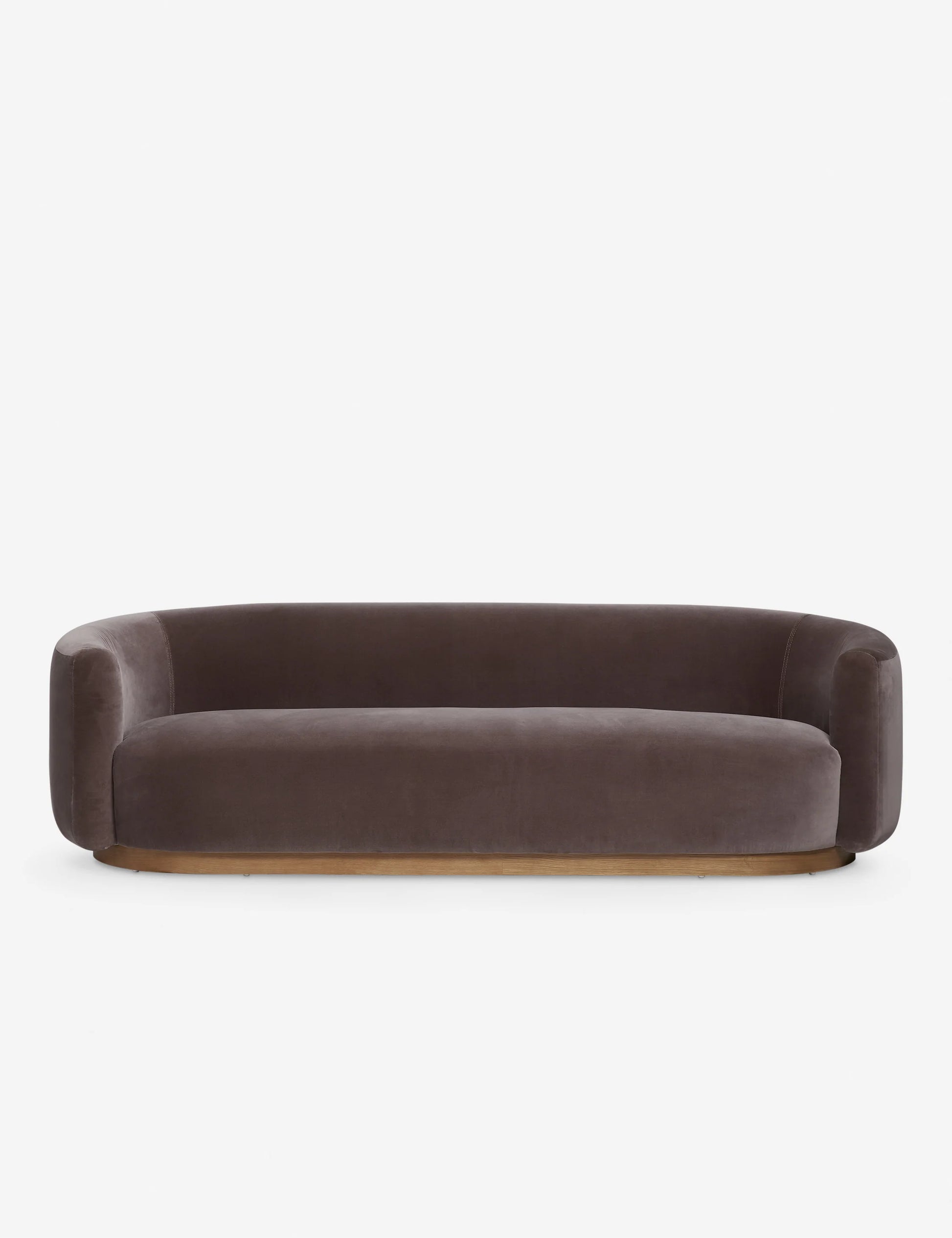 The Lowry Sofa is a stylish piece with its dark gray velvet upholstery, rounded arms, and low backrest. Set against a plain white background, it boasts a sleek, minimalist design with a wooden base that gives it an elegant and contemporary appearance.