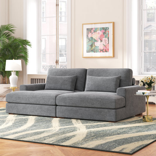 A cozy living room featuring the Etta Avenue Mordecai 90'' Square Arm Sofa in gray, complemented by a striped rug and a small side table with a lamp. A large plant is positioned beside the window, while a framed floral painting decorates the wall, illuminated by natural light streaming through tall windows.