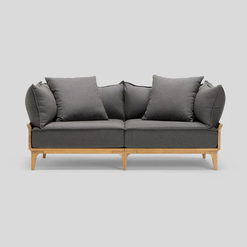 The Bluff Loveseat is a contemporary gray two-seater sofa featuring wooden legs and three large cushions, presented against a simple gray backdrop.