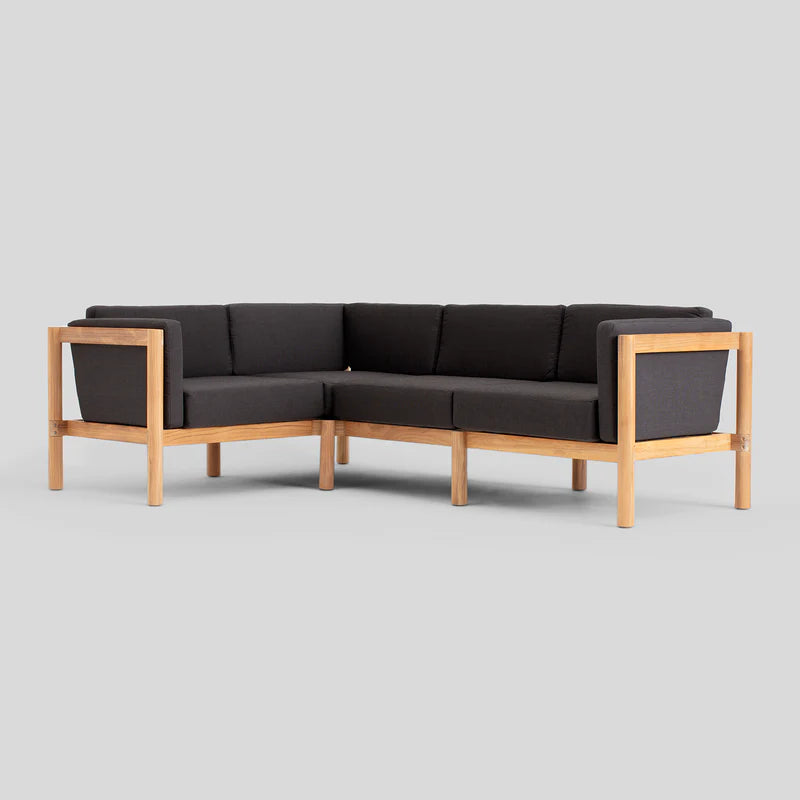 The Haven Sectional features a sleek L-shaped design with a wooden frame and dark gray cushions, set against a plain gray background.