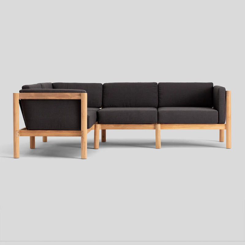 The Haven Sectional, a contemporary L-shaped sofa with a wooden frame and dark gray cushions, is set against a plain gray backdrop.