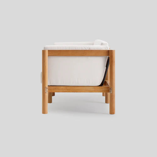 Side view of the Haven Sofa, a modern wooden armchair with white cushions set against a light gray background. It boasts a minimalist design with a sturdy wooden frame and legs.