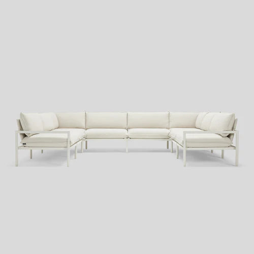 The Terra Sectional, a minimalist L-shaped white sofa, is displayed against a light gray background. It boasts clean lines, a metal frame, and plush cushions for a modern and contemporary appearance.