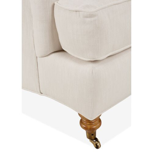 Close-up of the Brooke 6-Piece Left-Facing Sectional's corner, showcasing its cushioned beige upholstery. The base includes a wooden leg equipped with a brass caster for easy mobility.