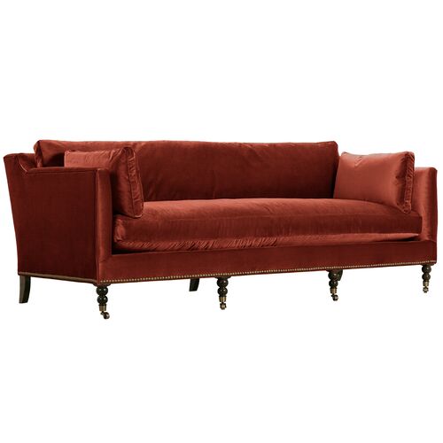 Introducing the Margot Velvet Sofa: a luxurious deep red velvet piece with a high back and low arms. This elegant sofa boasts ornate, dark wooden legs and slightly loose matching red cushions for enhanced comfort.
