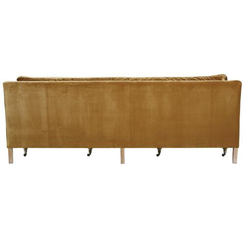 Back view of the Margot Velvet Sofa in mustard yellow, featuring wooden legs and castor wheels. This sofa boasts a sleek, modern design with a straight backrest and clean lines.