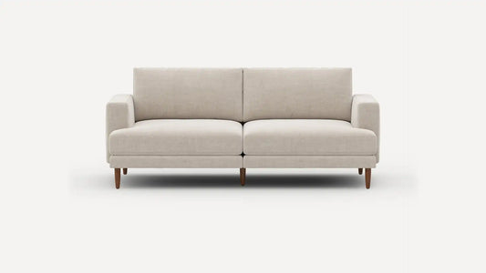 Introducing the Ember Mid-Century Modern 75" Sofa— a contemporary light beige piece showcasing clean lines and a minimalist design. This sofa features two seat cushions and two back cushions, complemented by low armrests and wooden legs, all set against a plain white background.