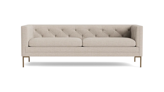 The Sit Tight 90" Sofa, featuring a beige tufted design with two cushions, is showcased against a solid black backdrop. Its minimalist aesthetic and wooden legs blend elegance with simplicity.