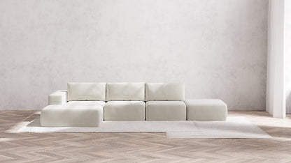 In a minimalist living room, the Modular 3-Seater Open-End Chaise Sectional in Boucle Aspen takes center stage atop a light area rug. The floor showcases a herringbone wood pattern, while the plain, light gray wall in the background enhances the airy and serene ambiance of the space.