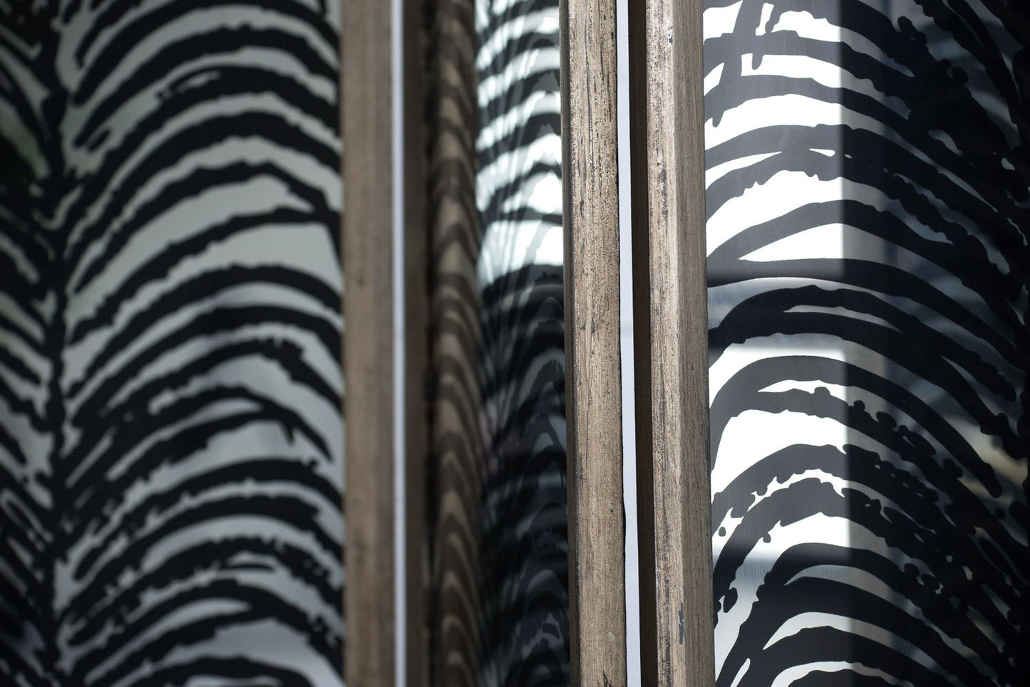Close-up of a glass window with a wooden frame, reflecting the bold black and white pattern of the Herero 4 Panel Decorative Screen Room Divider on both sides of the glass.