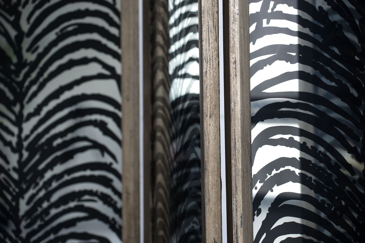 Close-up of a glass window with a wooden frame, reflecting the bold black and white pattern of the Herero 4 Panel Decorative Screen Room Divider on both sides of the glass.