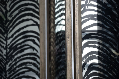 Close-up of a glass window with a wooden frame, reflecting the bold black and white pattern of the Herero 4 Panel Decorative Screen Room Divider on both sides of the glass.