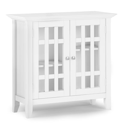 The Bedford Storage Media Cabinet is a white wooden cabinet with two glass-paneled doors featuring vertical slats, silver round knobs, interior shelves, and a modern minimalist design.