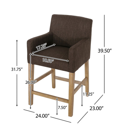 The Charmed Upholstered Counter Stool with H Frame Base and Round Arms is shown in brown with wooden legs. Dimensions: seat 18.5"W x 17.5"D, total height 39.5", seat height 26", arm height 31.75", depth 23", width 24", footrest at 11.25".