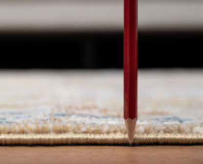 A red pencil stands vertically with its tip touching the edge of the Noble - GC_GEN7008 Area Rug, which rests on a wooden floor; focus is on the pencil and rug edge, with a blurred background.
