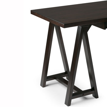 A close-up of the Sawhorse - Handcrafted Desk features a dark wooden rectangular top and sturdy, angled legs with horizontal supports, set against a plain white background.
