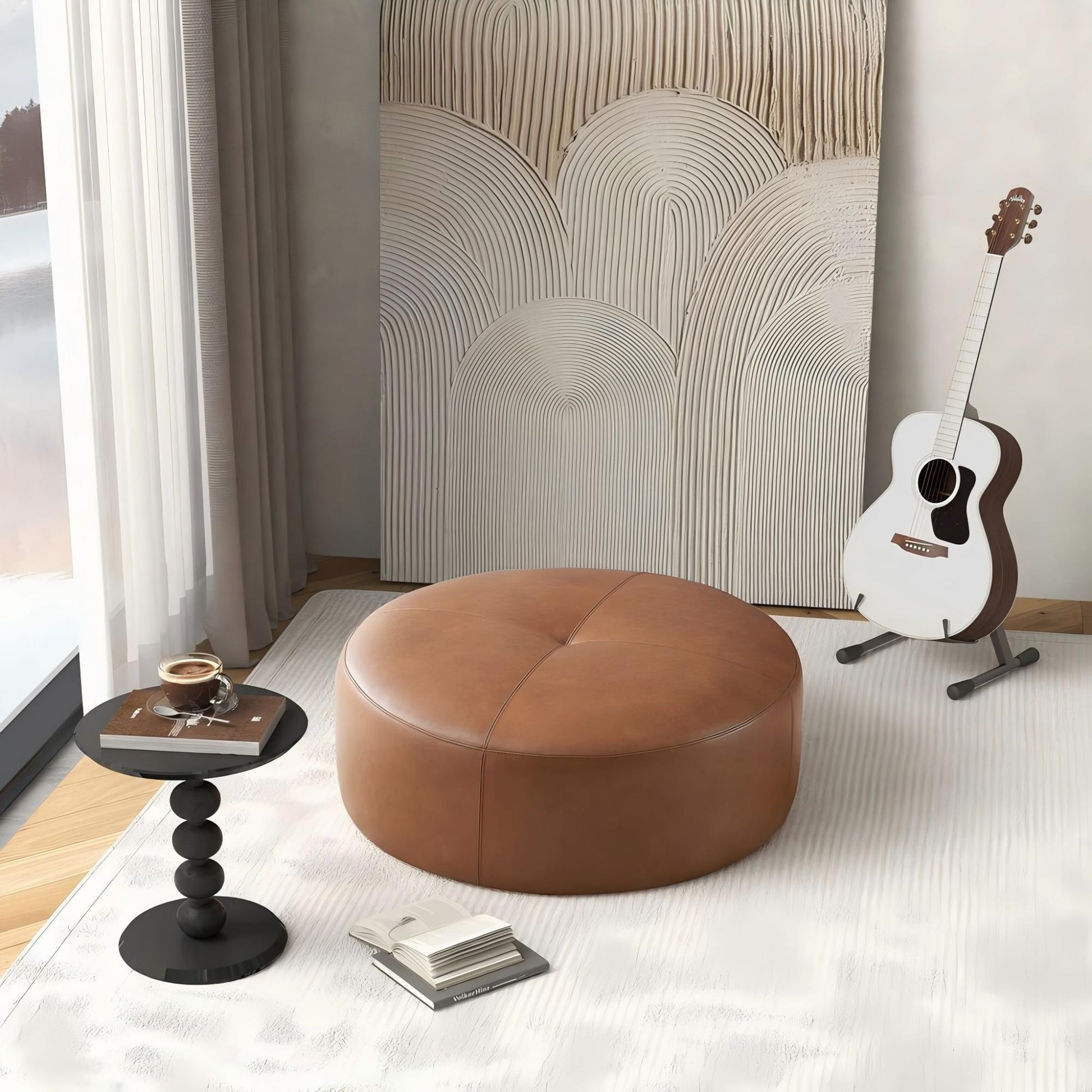 A cozy room featuring the Rochelin Ottoman in tan, a small black side table with a drink and book, abstract wall art, and an acoustic guitar on a stand by a window with sheer curtains.