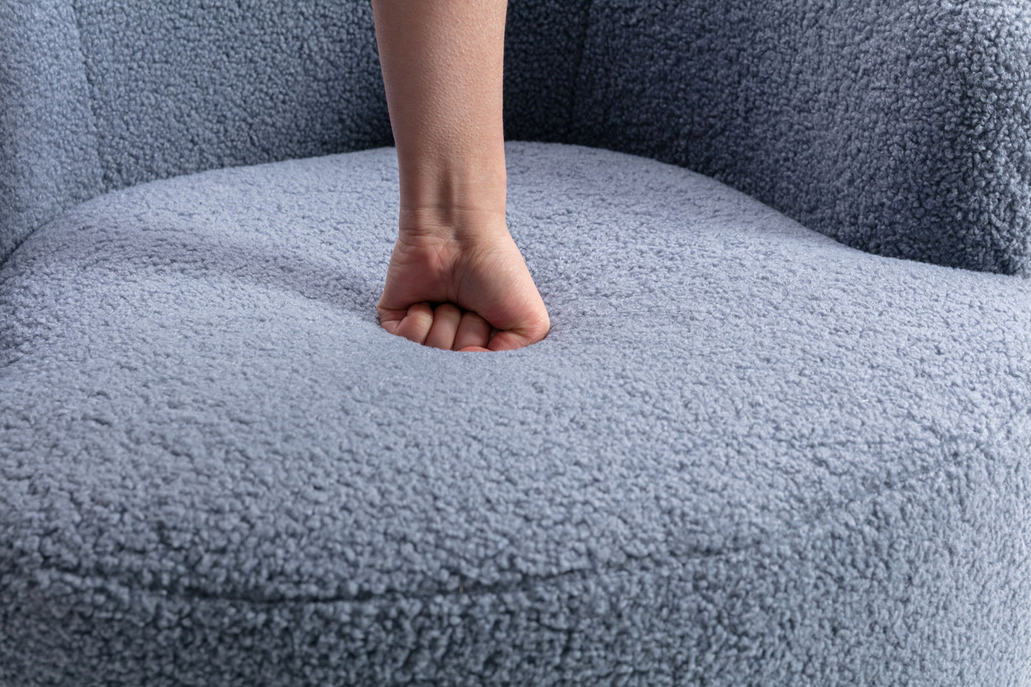 A person presses their fist into the cushioned seat of the Teddy Fabric Swivel Accent Armchair Barrel Chair With Powder Coating Metal Ring, creating a visible indentation in its soft, light gray upholstery.