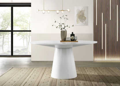 A modern dining room featuring the Jasper - Wide Contemporary Round Dining Table, decorated with a vase of branches and bottles on a tray. Pendant lights hang above, with large windows, wall art, and a beige patterned rug in the background.