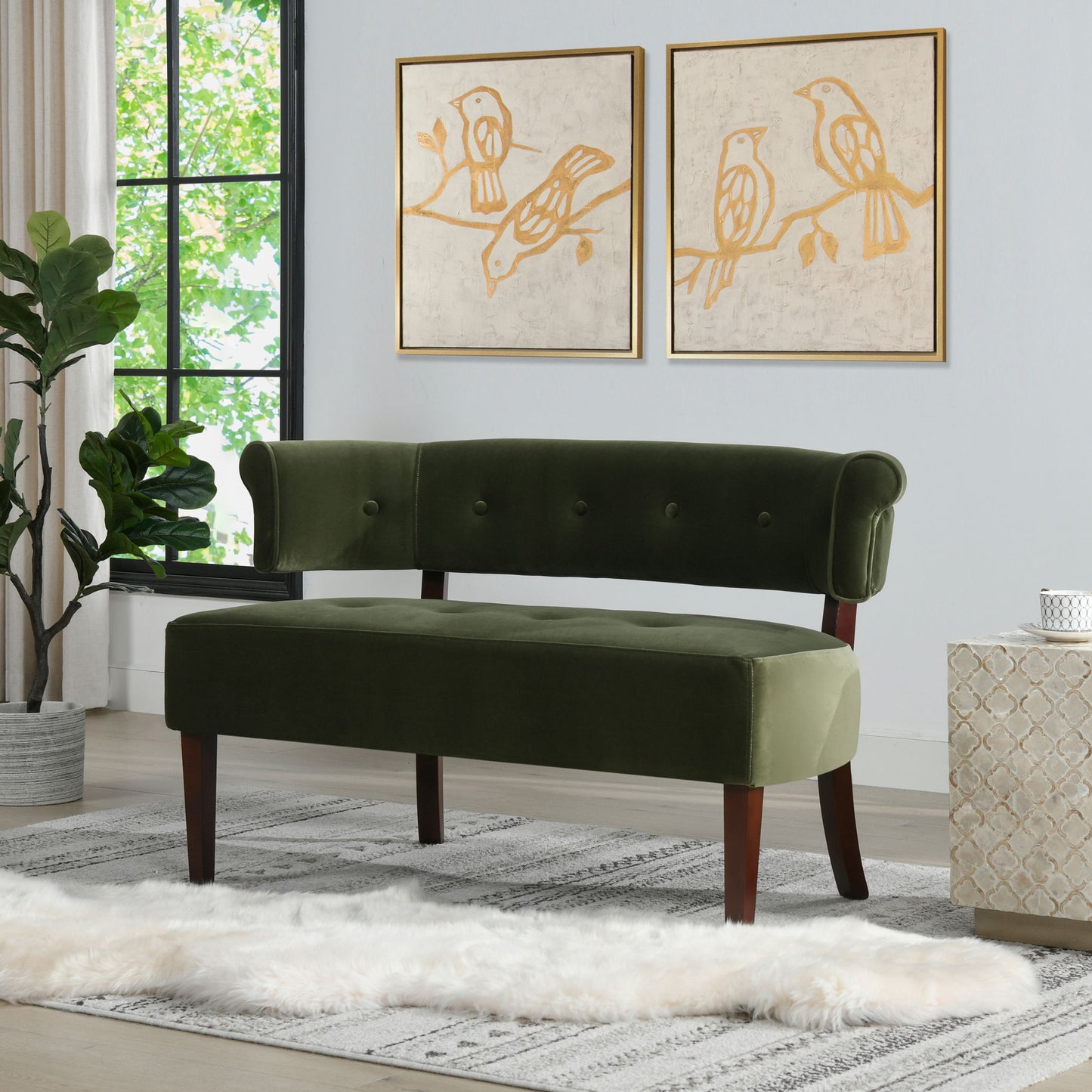 A modern living room featuring the Jared - Versatile Roll Arm Tufted Bench Settee in green velvet, a white furry rug, patterned rug, large window, bird-themed wall art, a plant, and a small textured side table.