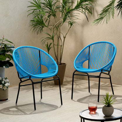 Two Nusa - Modern Chair Outdoor Seating pieces in blue with black metal legs sit on a light floor amid potted plants. A small round table holds a glass of red drink and a bowl, creating a cozy indoor atmosphere.