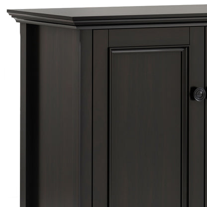 A close-up of the top corner of the Amherst - Wide 4 Door Storage Cabinet in Hickory Brown, showing its detailed trim, raised panel door, and a small round knob on the right side.