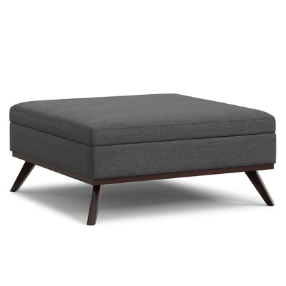 The Owen Multifunctional Square Coffee Table Storage Ottoman features dark gray upholstery, a cushioned top, and angled wooden legs with a dark finish.