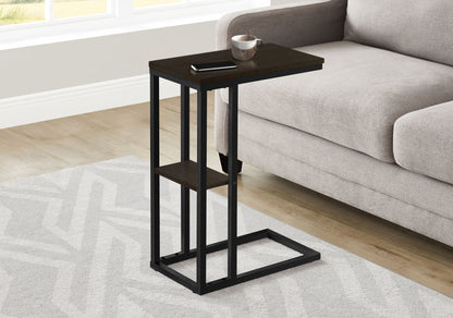 The Accent Table C-Shaped, Contemporary & Modern, with a dark wood top and black metal frame, sits beside a light gray sofa on a patterned rug in a bright room, holding a smartphone and cup.