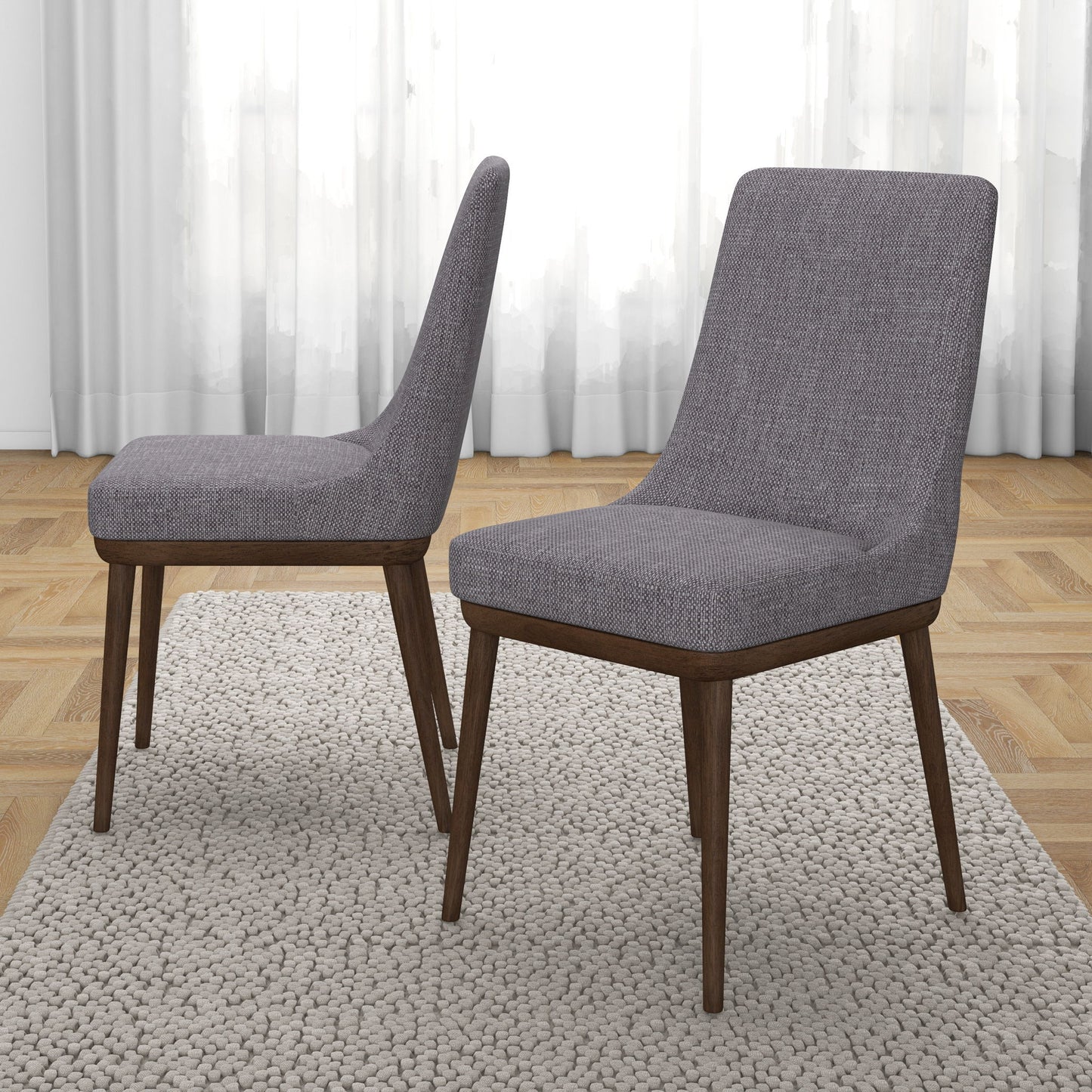 A set of two Kate Mid-Century Modern Dining Chairs with gray upholstery and wooden legs are placed on a textured light-colored rug, complementing the room’s light wood flooring and sheer white curtains.