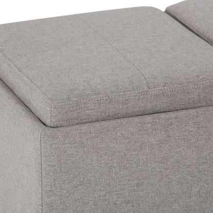 Close-up view of the Avalon Upholstered Storage Ottoman in light gray, featuring visible stitching and a removable cushioned top.
