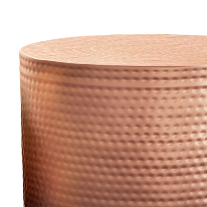 Close-up of the Nova Handcrafted Metal Side Table, featuring a cylindrical shape, copper finish, textured dimpled surface, and slightly uneven top edge. Lighting accentuates its metallic sheen and unique surface patterns.