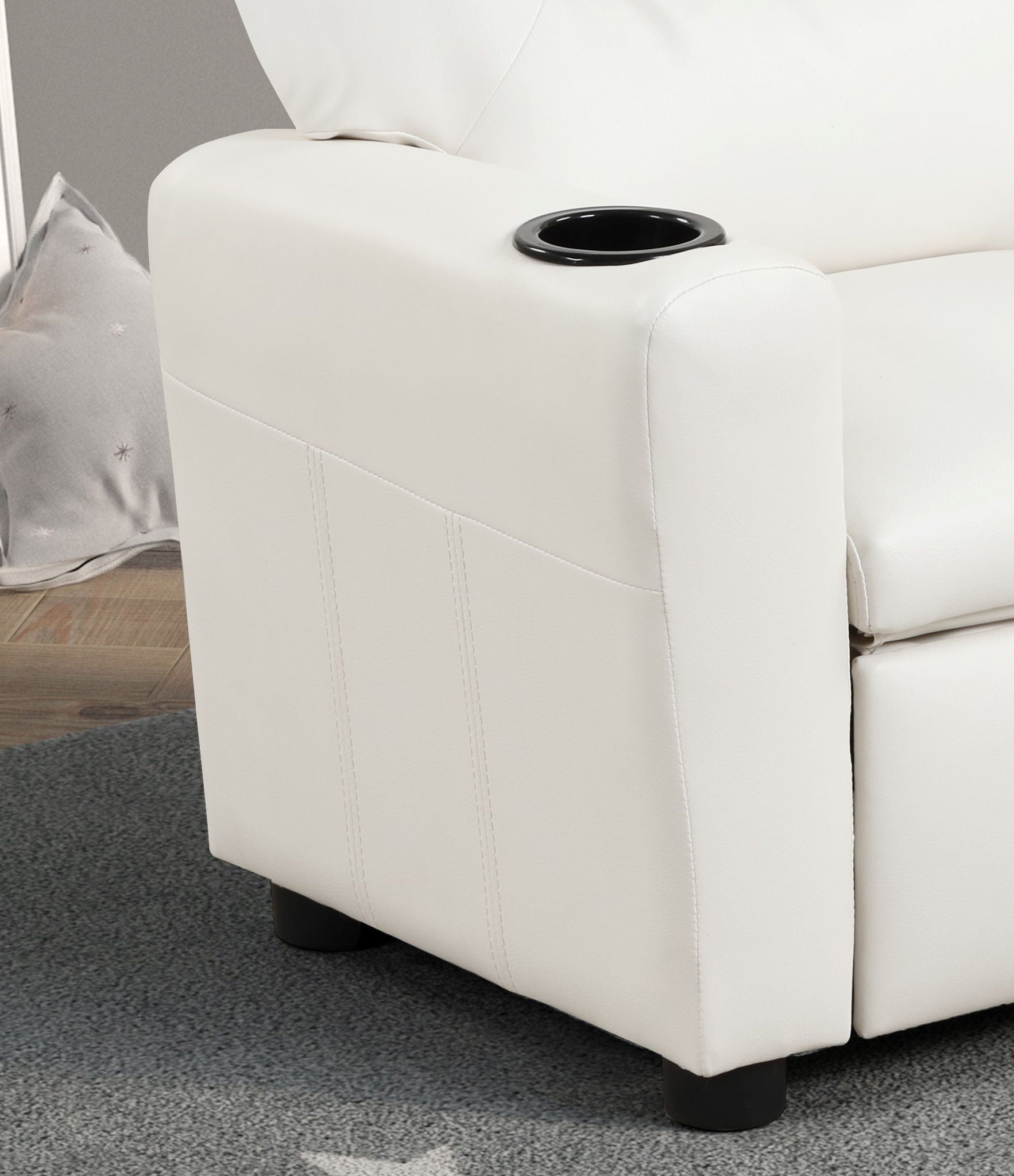 A close-up of the Marisa - PU Leather Kids Recliner Chair With Cupholder shows its modern white armrest with a built-in black cup holder, set on a gray carpeted floor. A pillow is partially visible in the background.