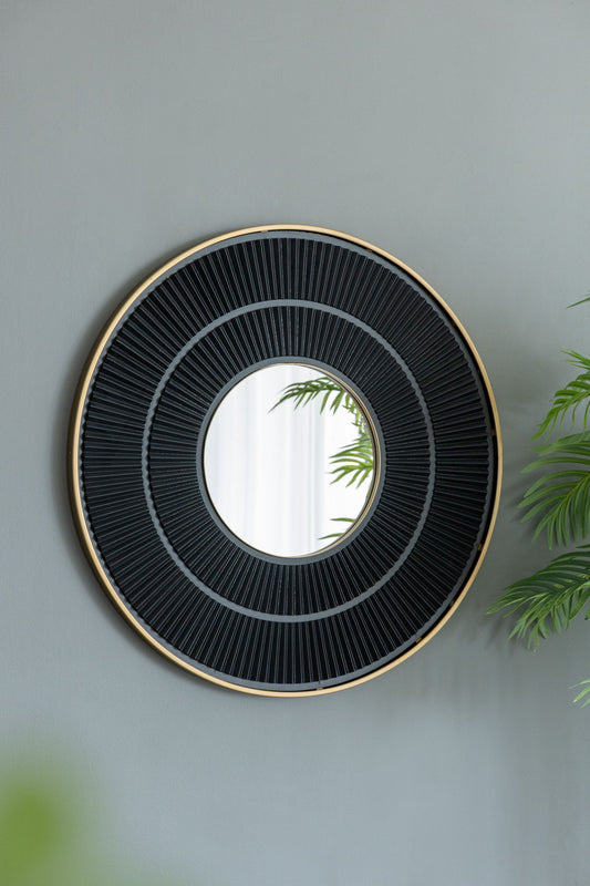 The Round Carter Wooden Mirror With Iron Frame in a neutral colorway hangs on a gray wall, framed by green leafy plants that reflect in the mirror's surface, adding light and natural beauty to your living space.