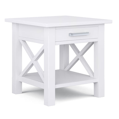 The Kitchener - Handcrafted Table is a white wooden end table featuring an X-shaped side design, one drawer with a silver handle, and an open lower shelf.