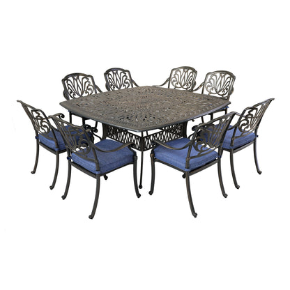 The Square 8 Person 64" Long Aluminum Dining Set With Cushions features a dark metal square table with ornate details and eight matching chairs with blue cushions, all displayed against a white background.
