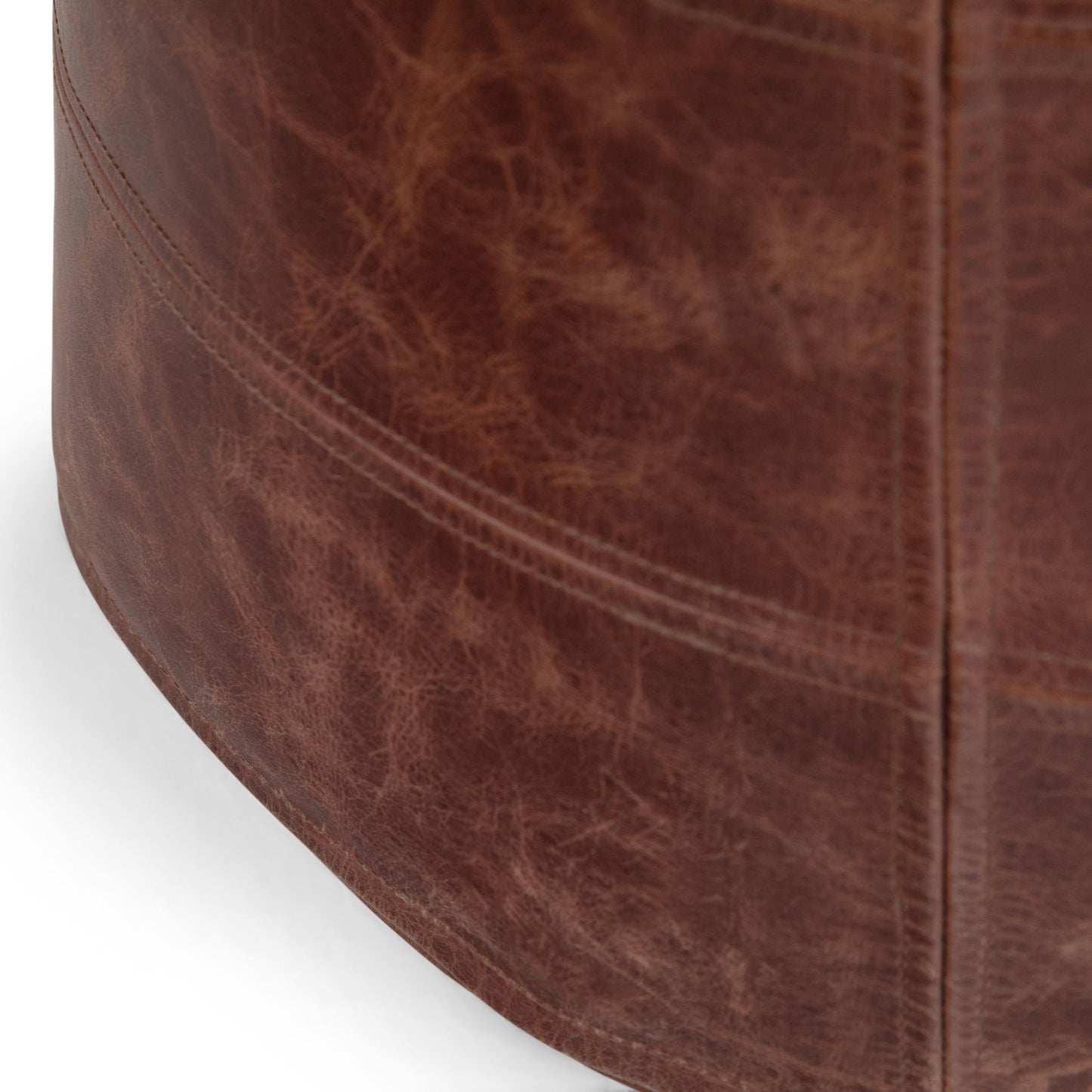 Close-up of the Connor - Handcrafted Round Pouf, featuring a brown leather surface with visible natural texture and stitching details.