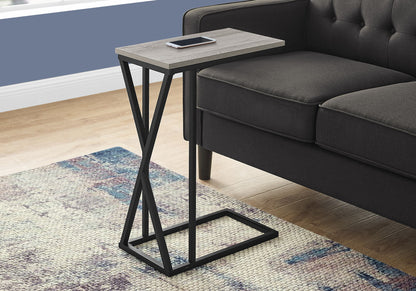 The Accent Table C-Shaped, Contemporary & Modern with a black metal frame and rectangular wooden top sits by a dark gray sofa, holding a smartphone. A colorful rug is partly visible on the wooden floor nearby.