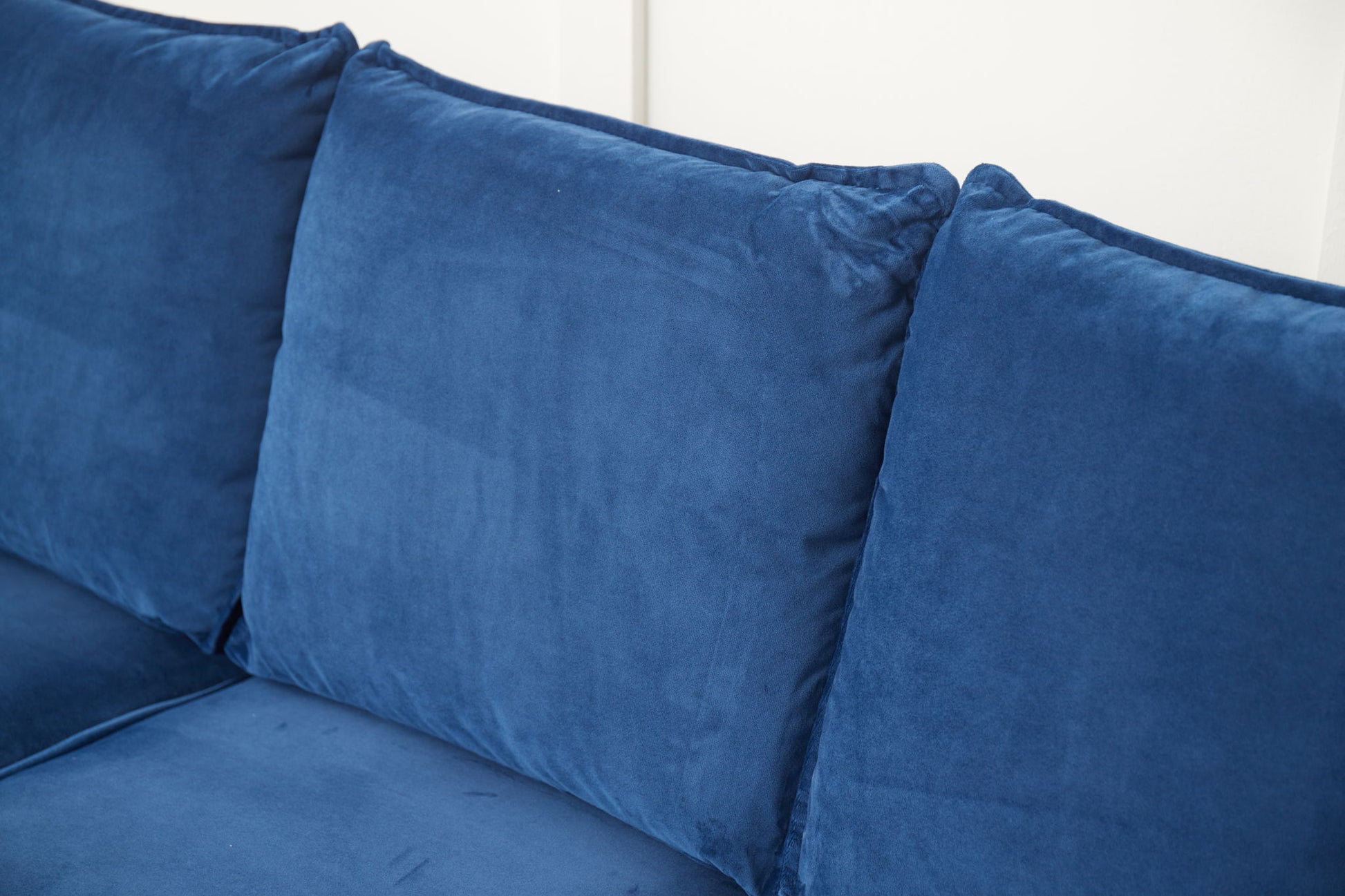 Close-up of the Graceful Design Plush Comfort Sofa in blue velvet, featuring three large, soft back cushions set against a white wall.
